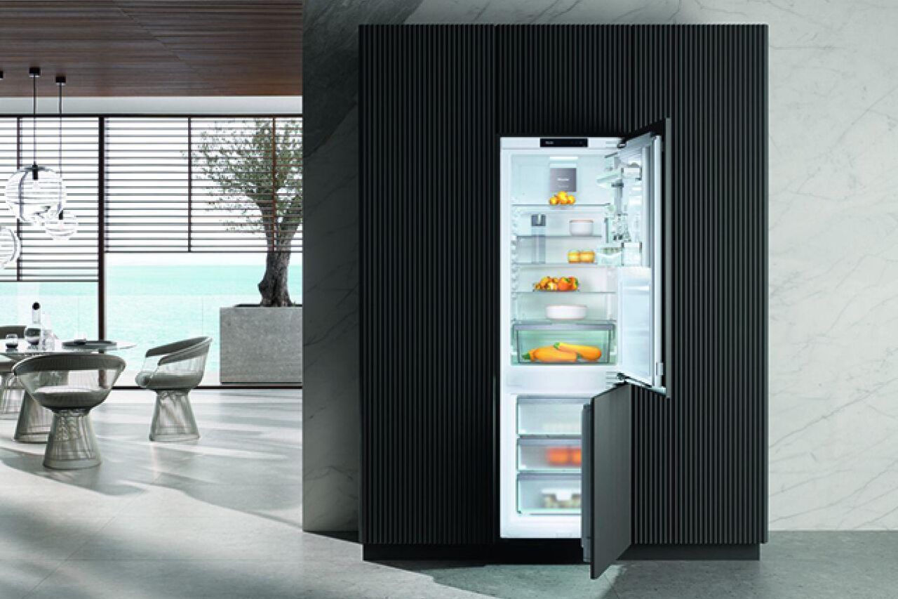 Een hedendaags interieur met op de voorgrond een Miele koelkast met onderaan een diepvries. De koelkast en diepvries staan open, zodat je de praktische binnenkant ervan kan zien.
