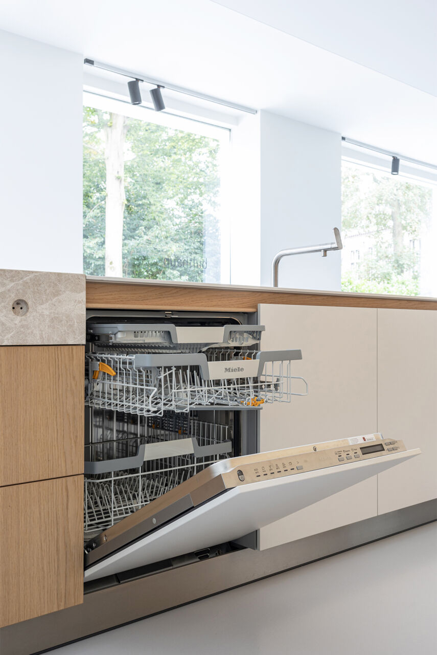 In de showroom van Van Damme Team in Sint-Denijs-Westrem zit een Miele vaatwas geïntegreerd in een hedendaagse keuken. Die werd uitgevoerd in wit laminaat en eikenhout. De vaatwaas staat gedeeltelijk open. De bediening zit bovenaan op de diepte van de deur.