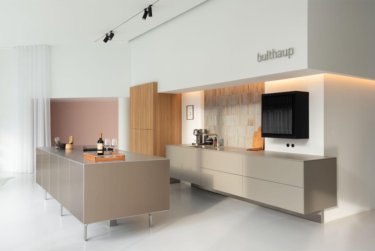 Grijze keuken in de showroom in Gent met fronten en werkbladen in laminaat kleur Flint. Met zwevende wandkasten en spoelbakken op maat ingewerkt in laminaat blad, enkel te zien bij bulthaup. Hoge kasten in massief eiken. Vaatwas op hoogte met push-to-open. Koelkast perfect fresh met push-to-open. Faience verticaal. Quooker kraan.