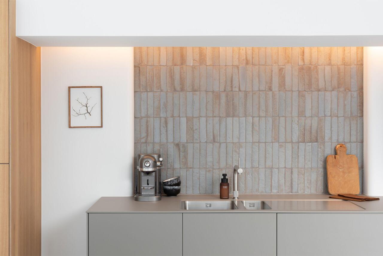 Grijze keuken in de showroom in Gent met fronten en werkbladen in laminaat kleur Flint. Met zwevende wandkasten en spoelbakken op maat ingewerkt in laminaat blad, enkel te zien bij bulthaup. Faience verticaal. Quooker kraan.
