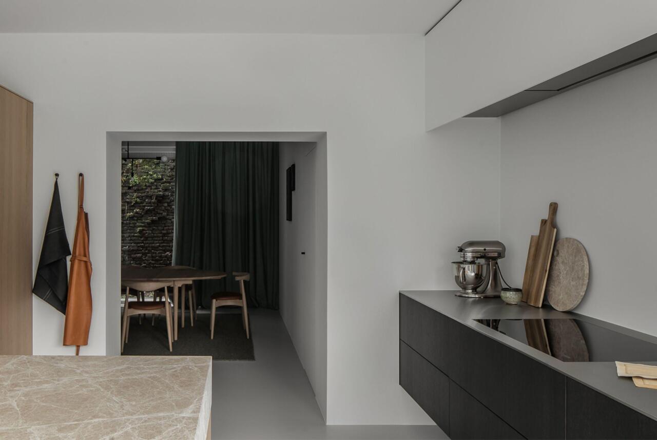 Een wandeling door de showroom met links een kookeiland met werkblad in dikke natuursteen. En rechts een zwevende kast in donker eikenhout met inductiekookplaat en verborgen dampkap erboven.
