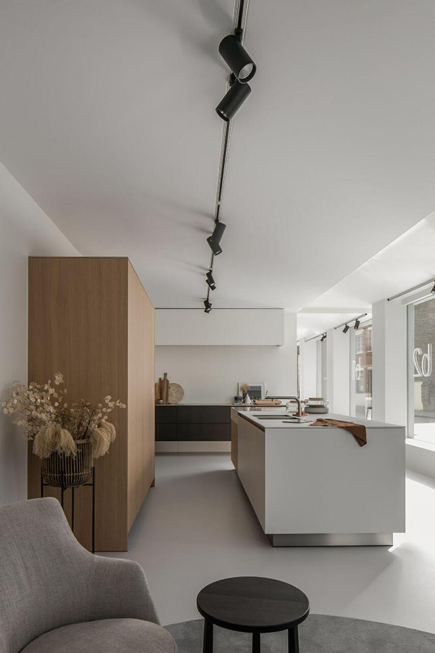 De showroom in Sint-Denijs-Westrem met meubilair van Carl Hansen and Son. Links hoge wandkasten in hout en rechts een kookeiland in wit laminaat.