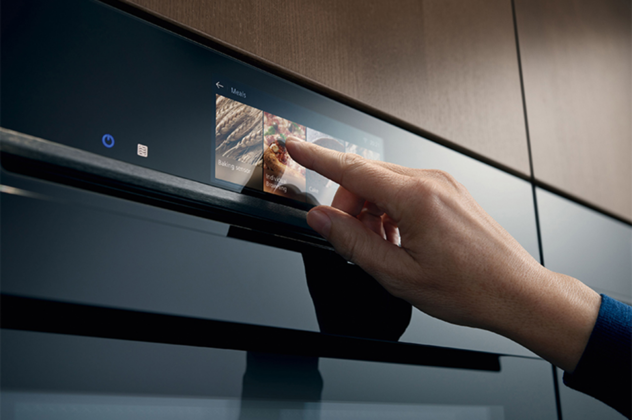 Een detail van een Siemens oven die door een hand ingesteld wordt via een touchbediening.