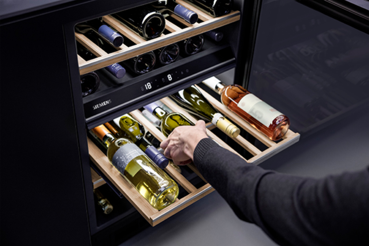 Een hand neemt een fles wijn uit een Siemens wijnklimaatkast.