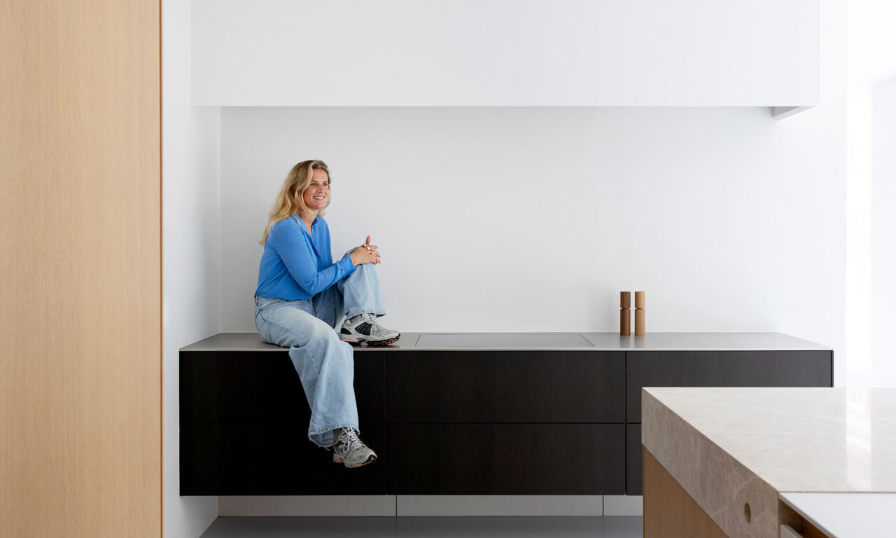 Sara Vanden Bossche zit op een donker houten keukenmeubel van bulthaup in de showroom in Sint-Denijs-Westrem.